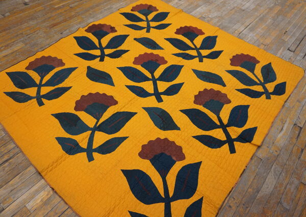 A flat, textured yellow textile with large maroon and dark blue floral motifs covers distressed wood planks.