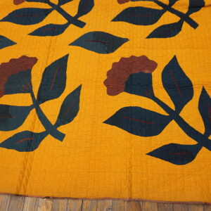 Mustard yellow textile rug with large teal leaves and maroon floral patterns rests on distressed wood flooring.