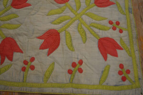 A quilted textile featuring appliquéd red tulips and green stems on a pale blue background.