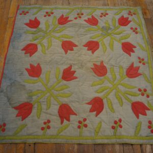 Flat quilted textile featuring red tulips and green leaves rests on distressed wood flooring.