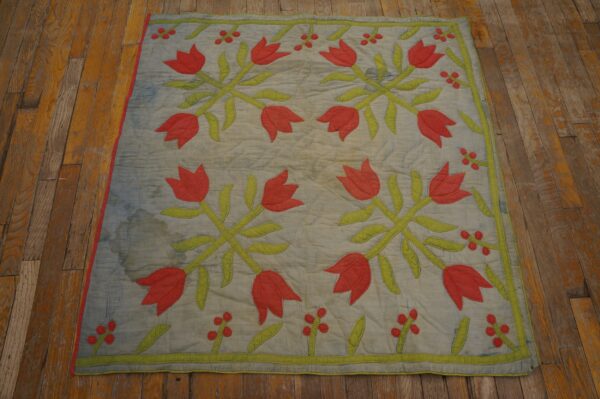 Flat quilted textile featuring red tulips and green leaves rests on distressed wood flooring.