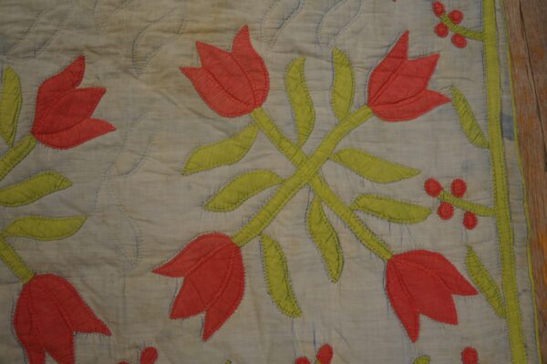 Appliqued red tulips and green stems on a quilted blue textile resting on wooden planks.