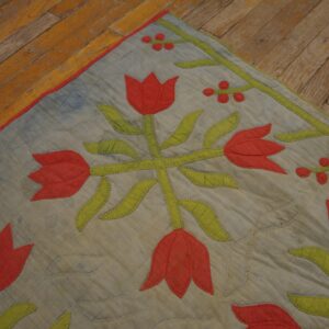 Stitched textile floor covering with red tulip and green leaf appliqué rests on distressed wooden planks.