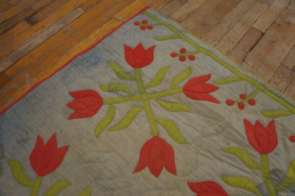 Stitched textile floor covering with red tulip and green leaf appliqué rests on distressed wooden planks.