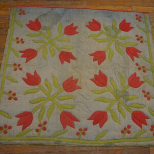 Quilted textile featuring faded blue background and red tulip floral pattern sits on rustic wood floors.