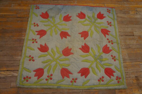 Quilted textile featuring faded blue background and red tulip floral pattern sits on rustic wood floors.