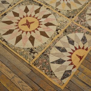 A quilted, flat textile with sunburst and floral patterns is placed diagonally on wide wooden planks.