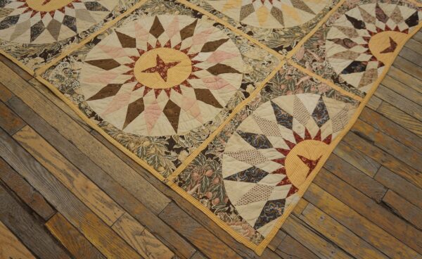 A quilted, flat textile with sunburst and floral patterns is placed diagonally on wide wooden planks.