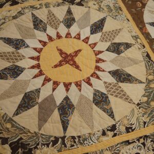 Close-up of a quilted textile with a central star medallion, surrounded by dark brown and cream floral borders on wood flooring.