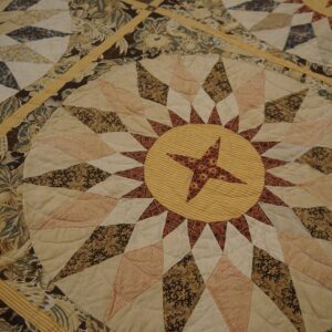 Close-up of a quilted rug with cream, brown, and yellow star medallion and floral patchwork patterns.
