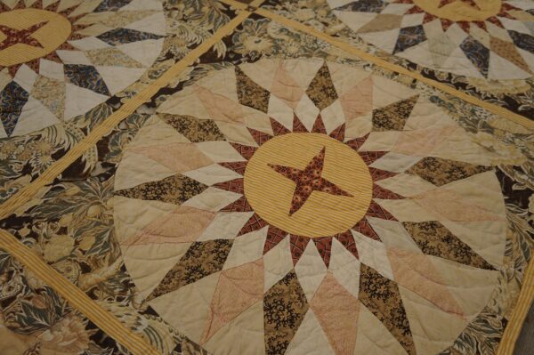Close-up of a quilted rug with cream, brown, and yellow star medallion and floral patchwork patterns.