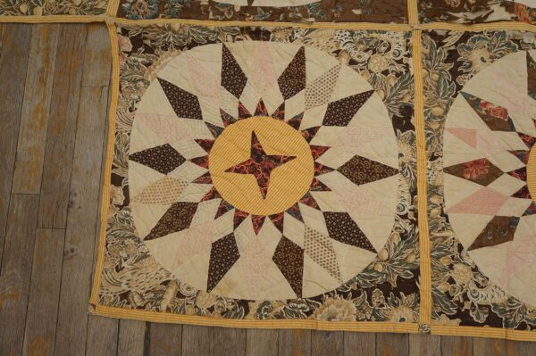 Quilted textile squares featuring brown floral borders and a central yellow and cream starburst pattern on wooden planks.