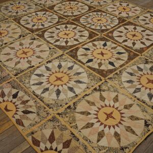 A large, flat, patched rug featuring repeated sunburst star medallions in brown, cream, and red tones on a distressed wood floor.