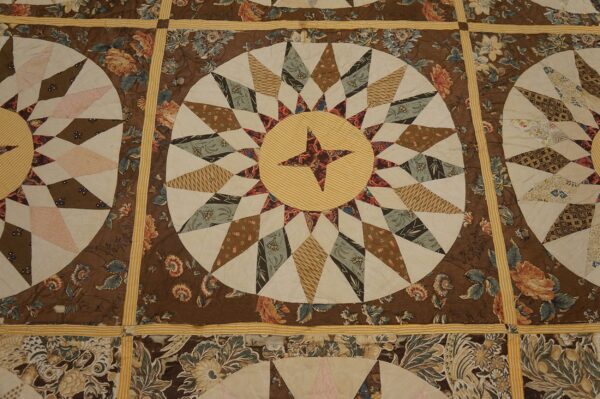 Brown, cream, and yellow textile featuring radiating star medallions framed by dark floral print blocks.