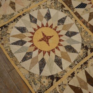 Patchwork textile featuring circular sunburst patterns and floral borders in cream, brown, and blue on wood floors.