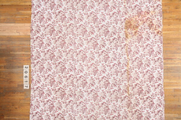 Cream rug with a repeating pattern of mauve grape bunches and leaves on a visible hardwood floor.