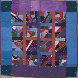 Square textile with crazy quilt patchwork squares framed by purple and blue borders with scattered knots.