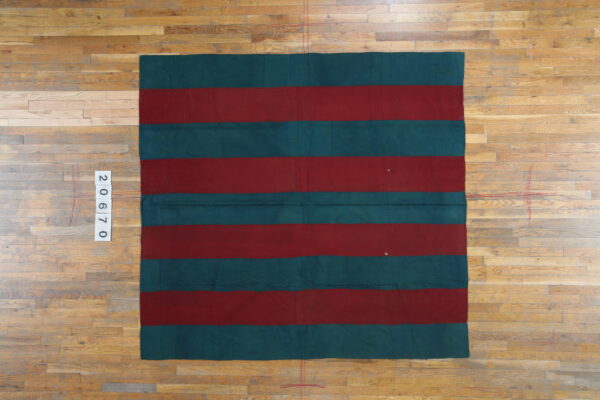 Deep red and dark teal rug with wide horizontal stripes displayed on natural wood plank flooring.