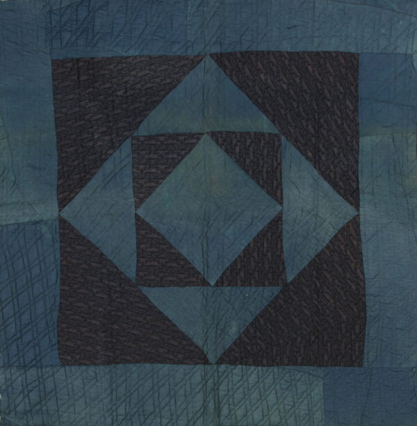Quilted textile with a geometric pattern in dark indigo blue and black, featuring detailed stitchwork texture.