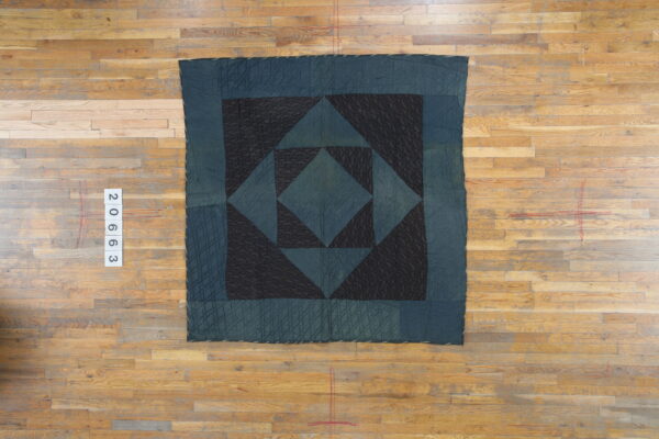 Quilted dark blue and black geometric rug featuring squares and triangles on light plank hardwood flooring.