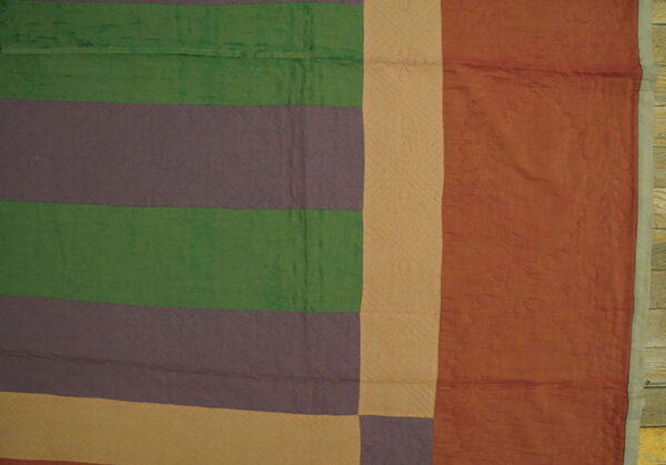 Quilted textile featuring wide stripes of green, purple, tan, and rust colors with visible patterns.