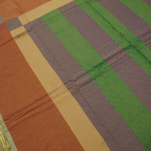 Quilted rug with thick stripes in rust, purple, green, and tan colors resting on distressed wood floors.