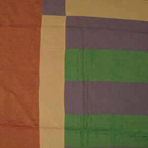 Rust, tan, purple, and green color blocks form a quilted textile lying on wood planks.