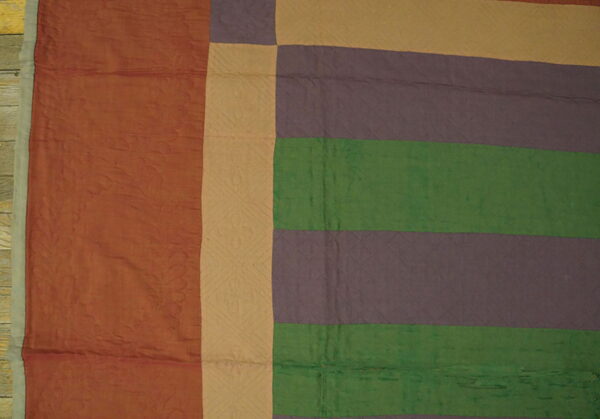 Rust, tan, purple, and green color blocks form a quilted textile lying on wood planks.