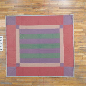 Block-patterned quilted textile in red, purple, and green, laid flat on worn wood plank flooring.