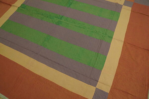 Geometric rug with wide green and gray stripes framed by yellow and terracotta color block patches.