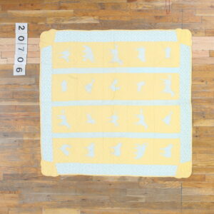 Yellow quilted fabric with blue animal patterns and a patterned border rests on wooden plank flooring.