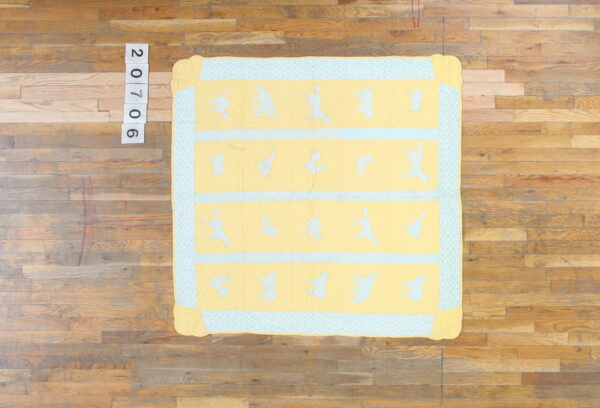 Yellow quilted fabric with blue animal patterns and a patterned border rests on wooden plank flooring.