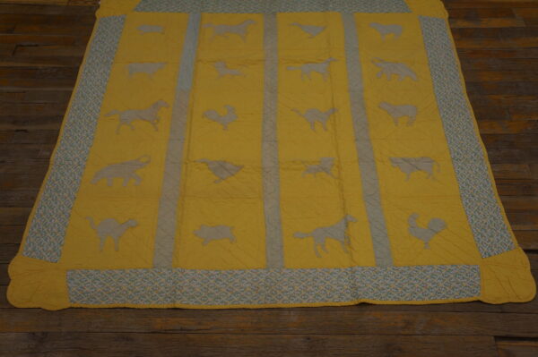 Quilted yellow area rug displays blue animal silhouettes and patterned borders on rustic wood flooring.