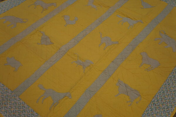 Wrinkled yellow and gray textile rug displaying diagonal stripes and silhouettes of various animals and a patterned border.