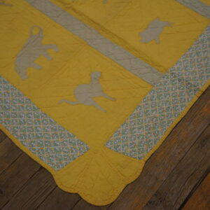 Bright yellow quilted textile with gray animal patches and a patterned border rests on dark wood planks.