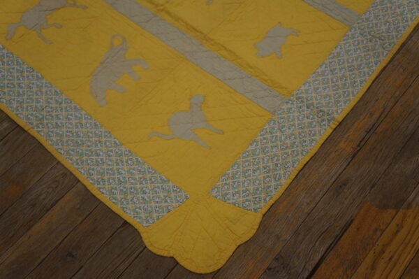 Bright yellow quilted textile with gray animal patches and a patterned border rests on dark wood planks.