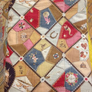 Low-pile textile with a complex diamond patchwork pattern in reds, blues, browns, and illustrative motifs on a wood floor.