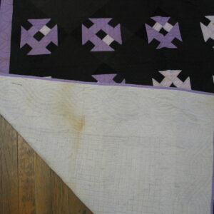 Black, purple, and white patterned textile lies on wood planks, exposing its stitched, discolored white backing.