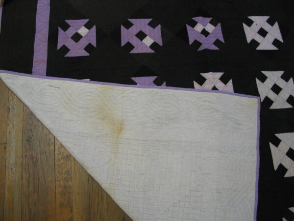 Black, purple, and white patterned textile lies on wood planks, exposing its stitched, discolored white backing.