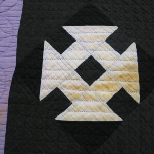Quilted black textile with a pale lavender stripe and a distressed white geometric pattern showing stains.