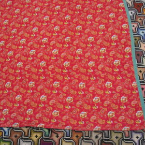 Red rug with yellow and green floral paisley motifs rests atop a geometric multicolor rug.
