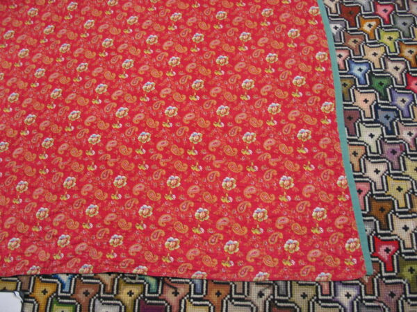 Red rug with yellow and green floral paisley motifs rests atop a geometric multicolor rug.