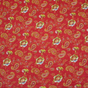 Red textile with repeating gold paisley, green leaves, and white and blue floral patterns.