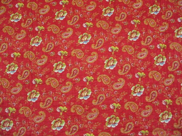 Red textile with repeating gold paisley, green leaves, and white and blue floral patterns.