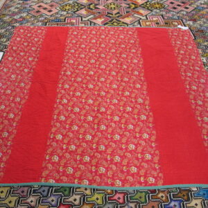 Red floral and solid textile covering a multicolored rug with large geometric patterns.
