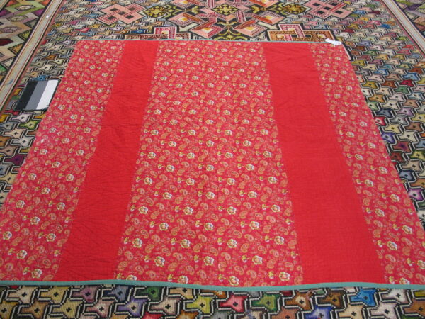 Red floral and solid textile covering a multicolored rug with large geometric patterns.