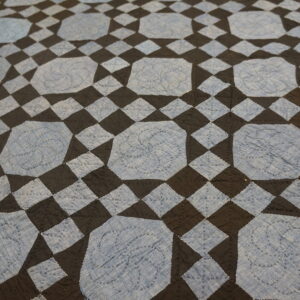 Low pile rug with a geometric pattern of light blue stitched octagons and dark checkerboard squares.