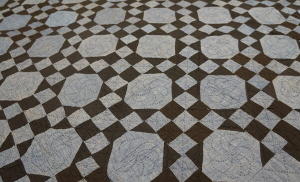 Low pile rug with a geometric pattern of light blue stitched octagons and dark checkerboard squares.