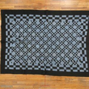 Black and light blue flatweave rug with a repeating checkerboard and octagon pattern on a light wood floor.
