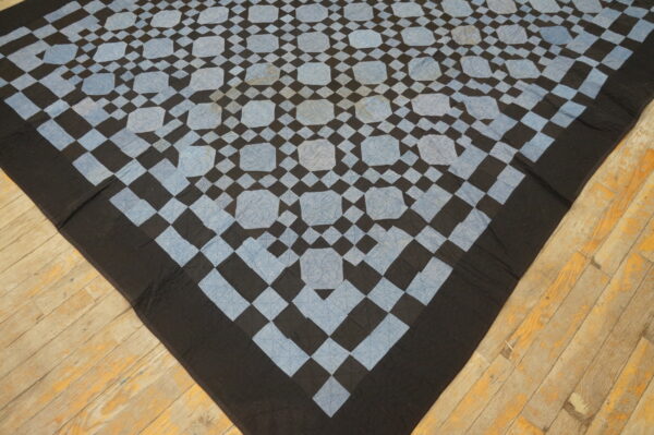 Low pile black and light blue geometric textile covers distressed diagonal wooden floorboards.